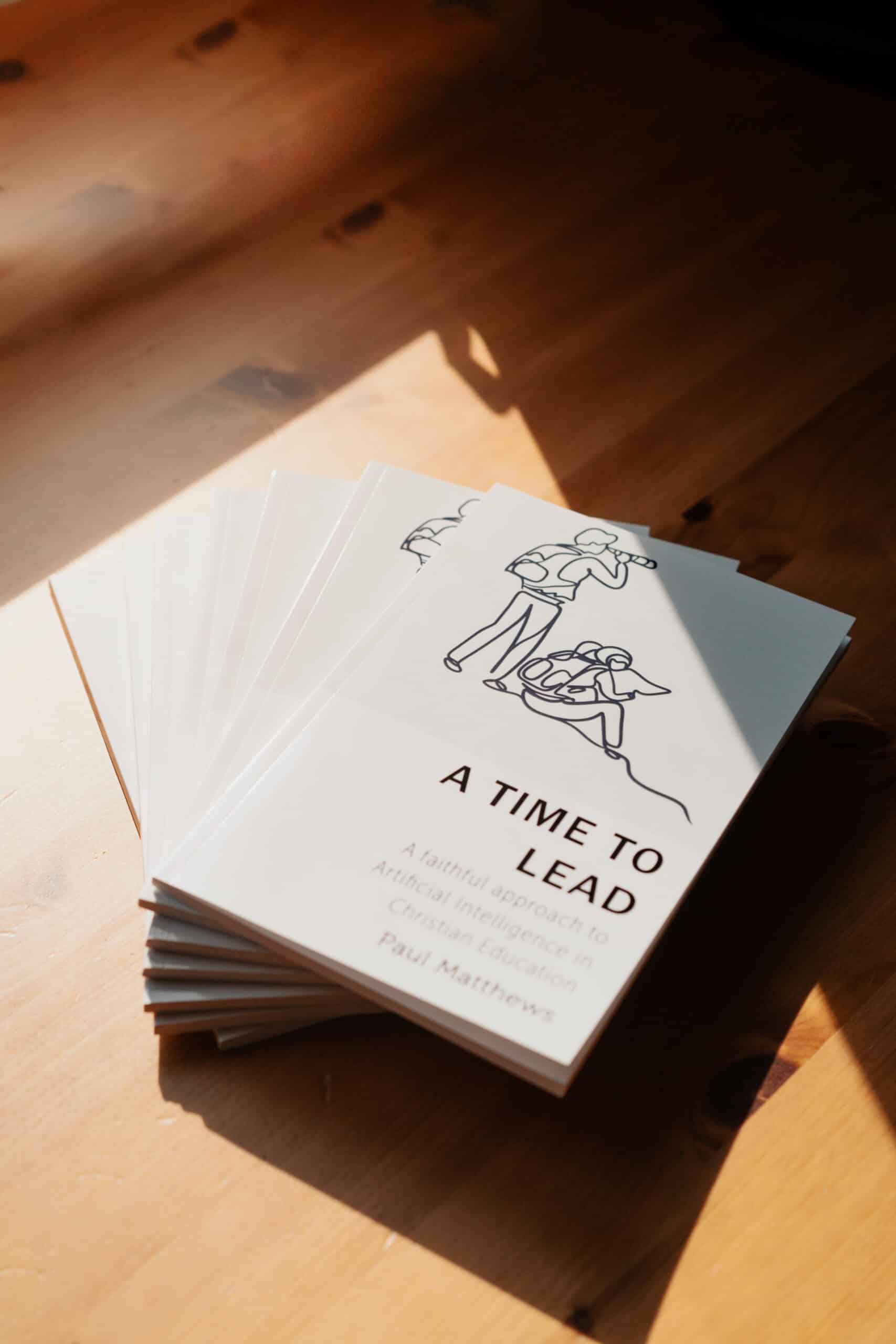 A stack of A Time to Lead: A Faithful Approach to AI in Christian Education book fanned out on a wood table in the sunlight
